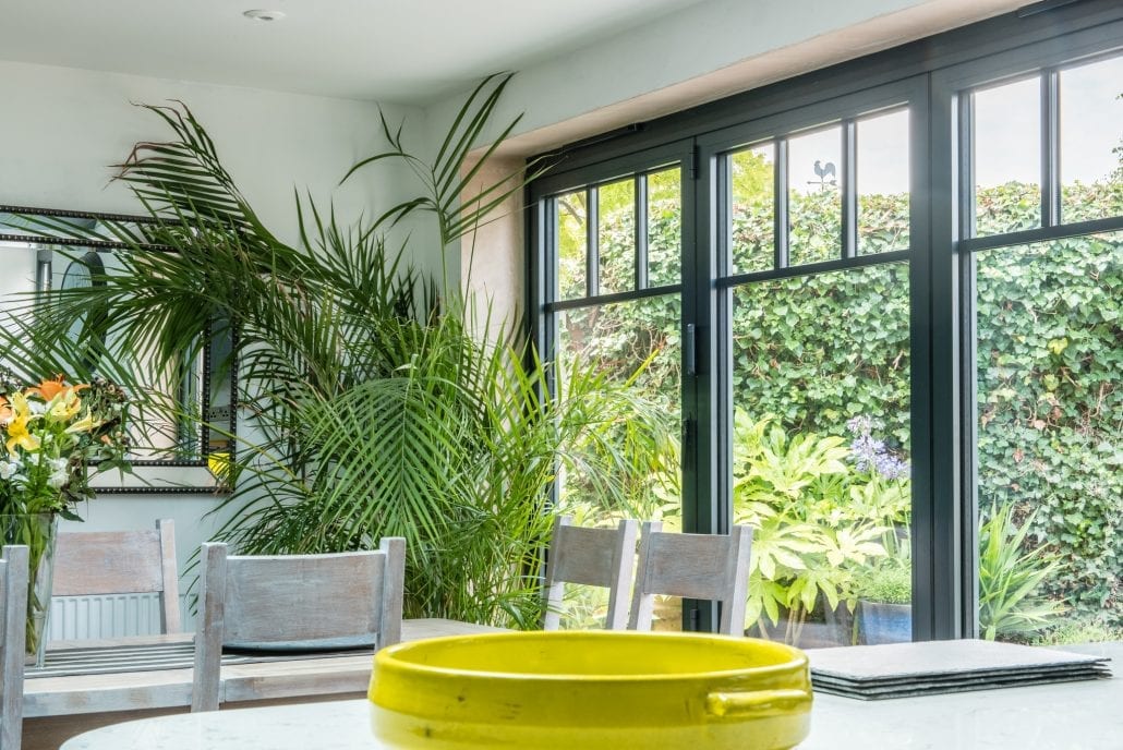 Custom aluminium bifold doors with solid lower panels and mullioned tops on an English cottage, opening to a courtyard garden
