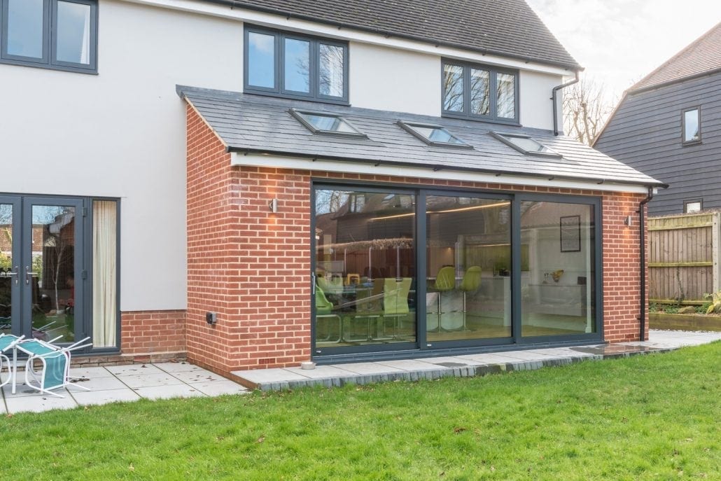 Large aluminium sliding doors along a lit open-plan interior at dusk