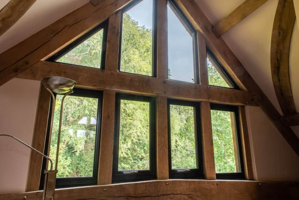 Dark aluminium door frame against rustic timber and cast-iron fittings in barn conversion