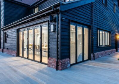 Night view of bifold doors and glazing on black feather-edge barn