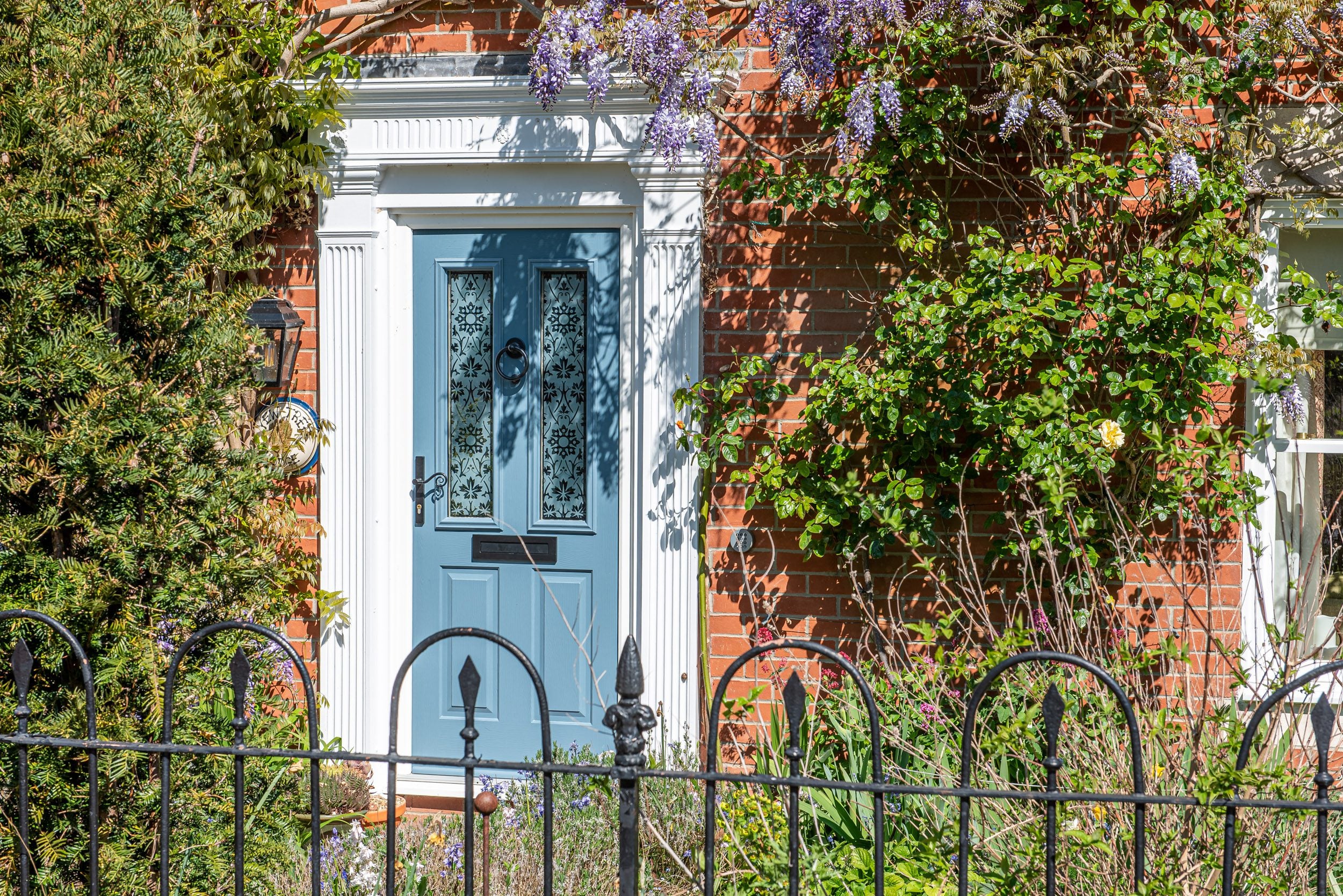Blue front door with leaded glass framed by wisteria and iron railings