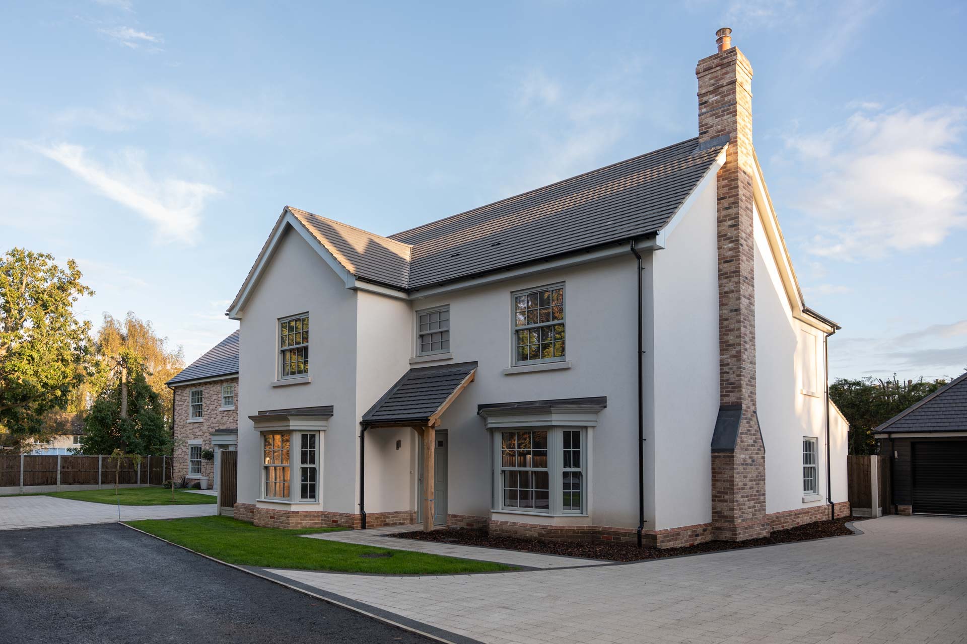 Rendered home with sage uPVC vertical sliding windows, bay windows and an oak porch, with a brick home behind