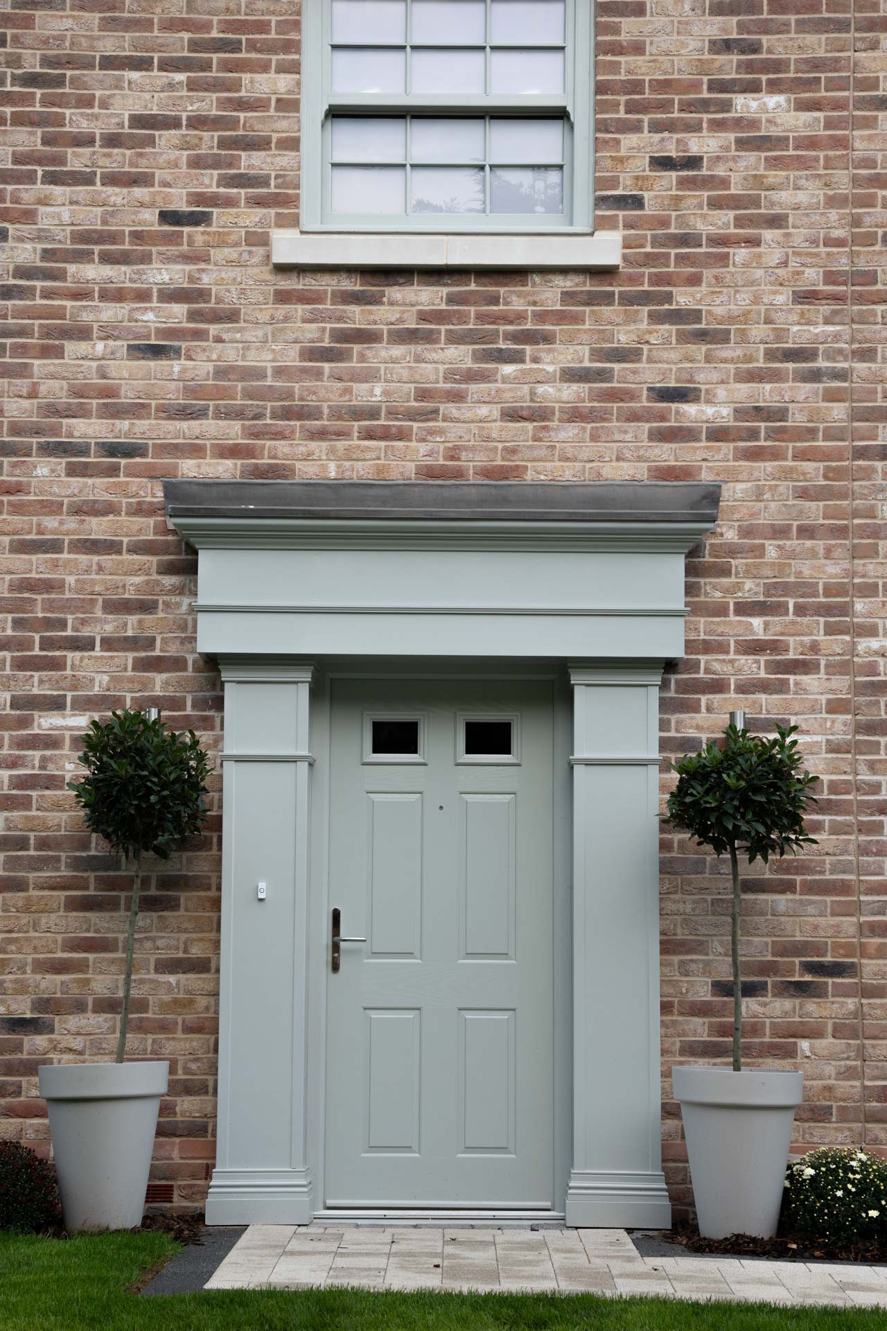 Sage composite front door beneath a portico, with a uPVC vertical sliding window above
