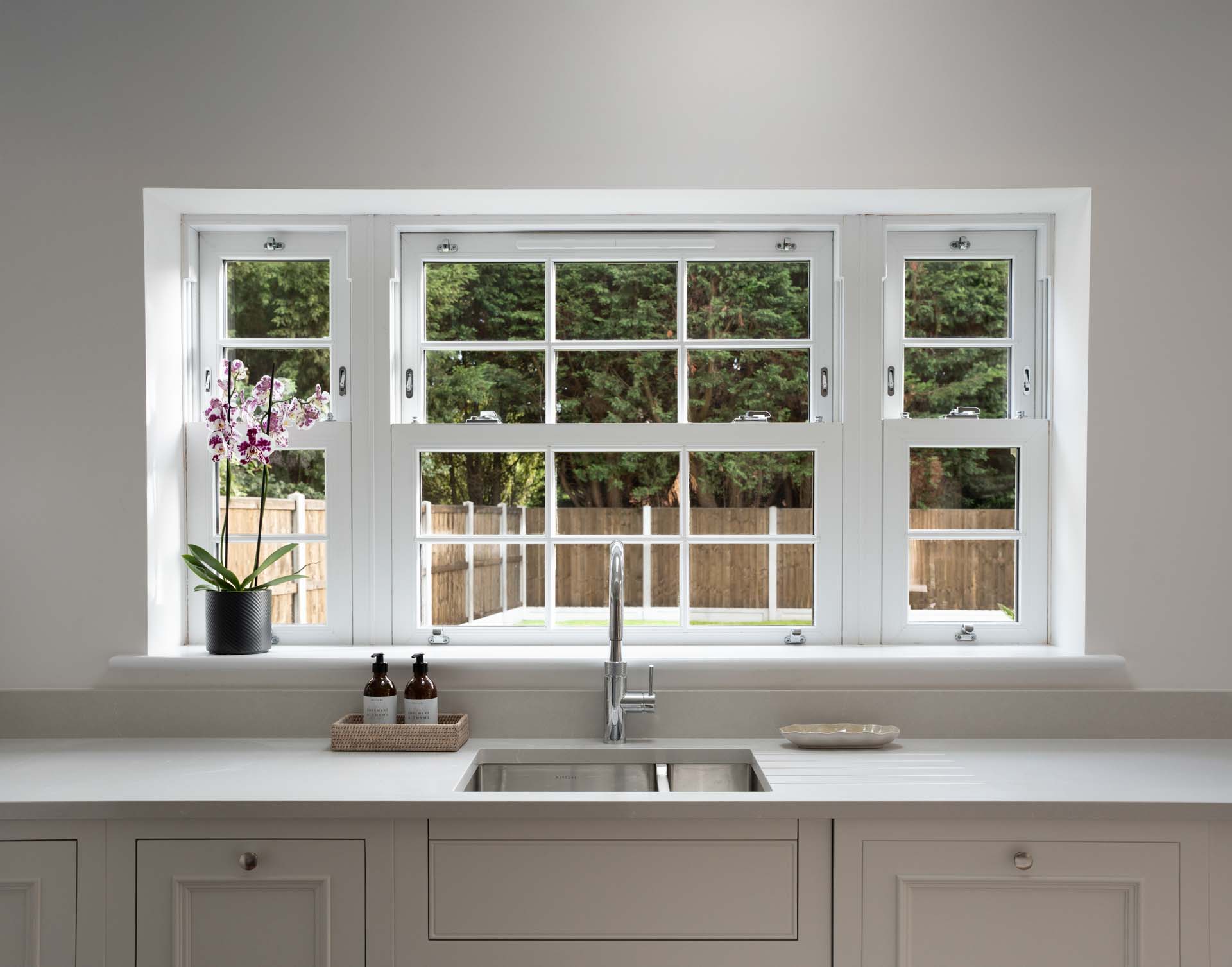Three white uPVC vertical sliding windows above a kitchen sink, seen from inside