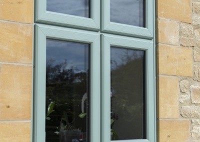 Close-up of a Deceuninck Heritage 2800 sculpted casement window in Chartwell Green against Cotswold stone