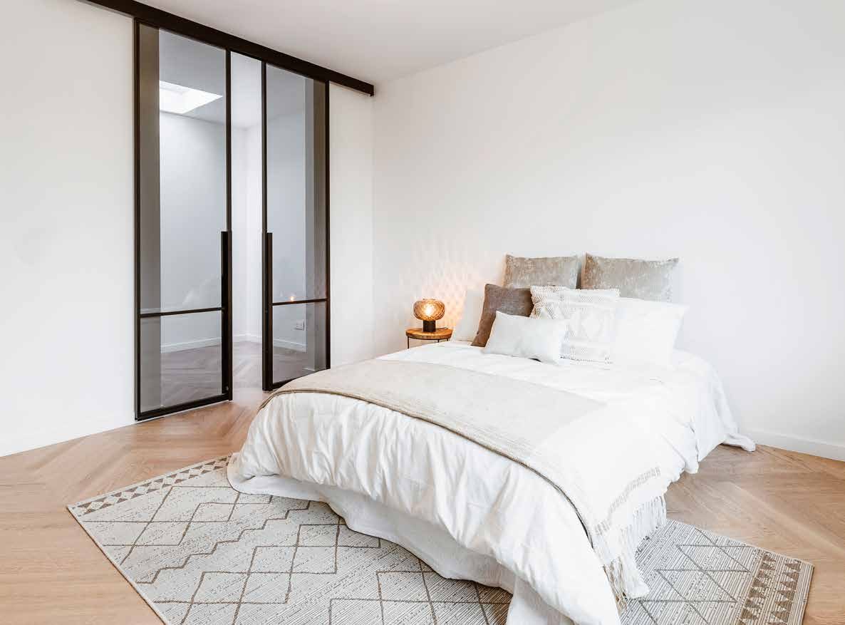 Black steel sliding door with clear glass beside a bed in a bright bedroom
